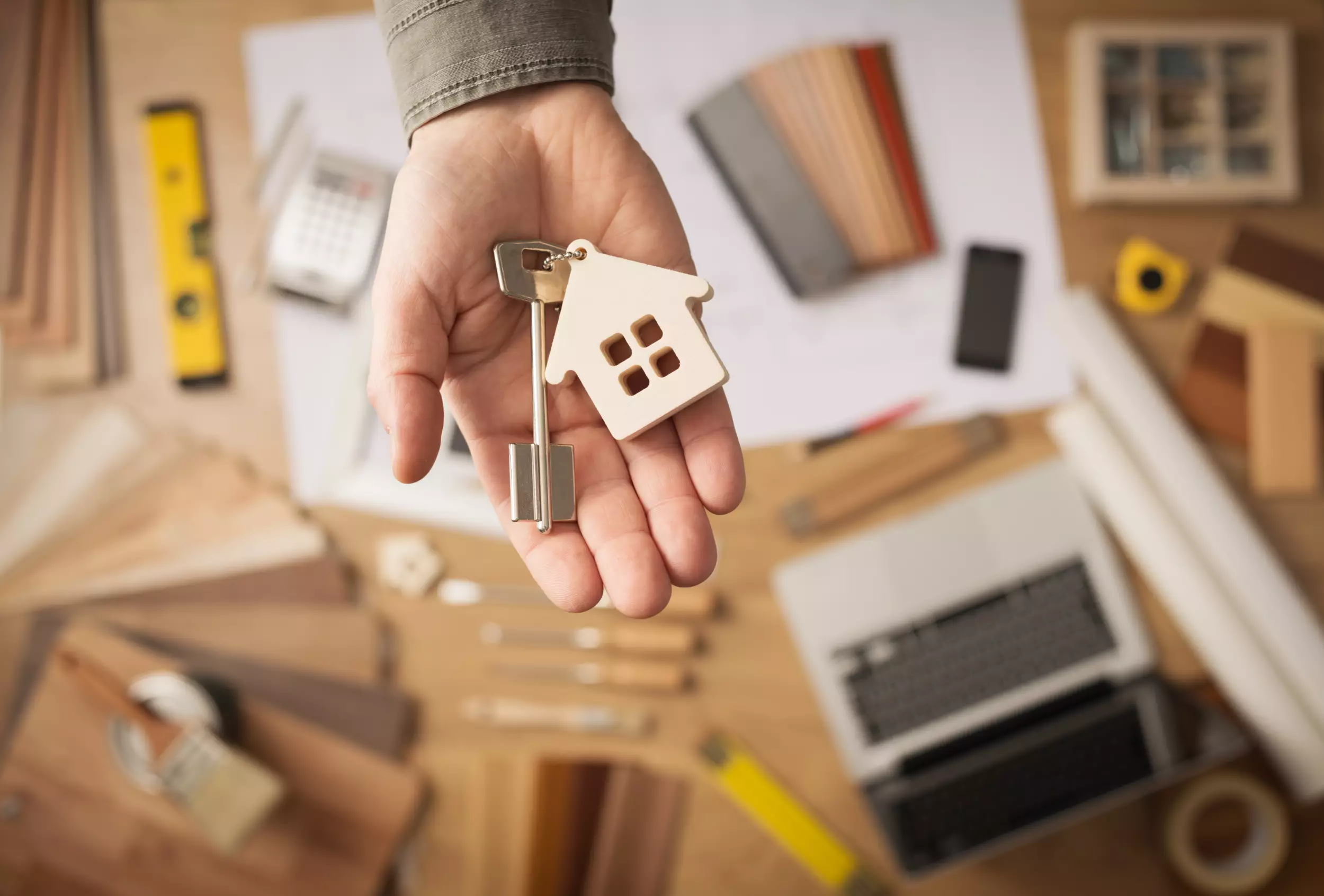 A hand holding house keys over a desk